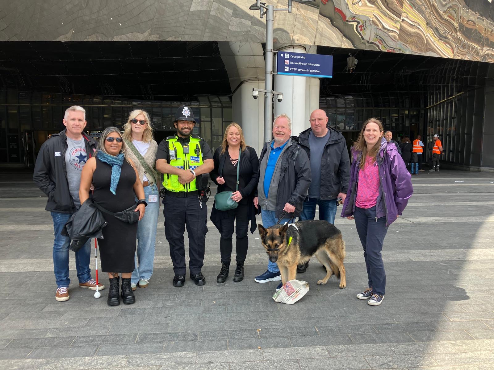 Members of Birmingham and Black Country SLC stood with staff fro West Midlands Police in plain clothes, as well as a policeman in a yellow high-visibility jacket. They are all facing the camera, smiling, in Birmingham City Centre.