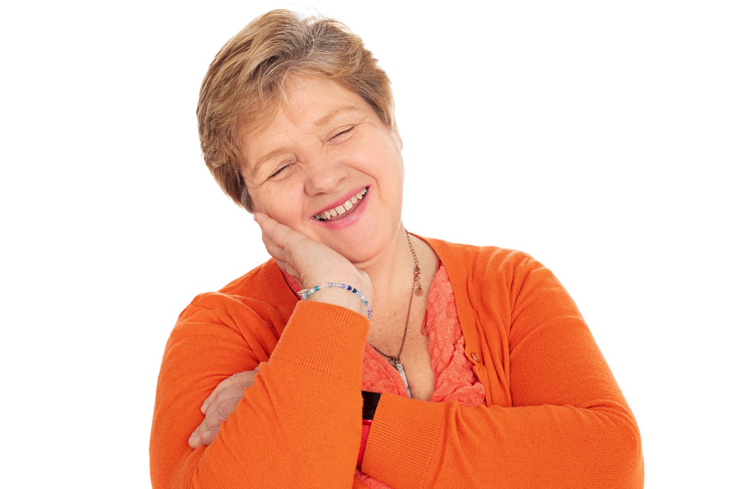 Anita Davies, Engagement Manager for Wales, pictured in a studio setting. She is wearing an orange cardigan and posed against a white wall. with one hand resting under her chin.