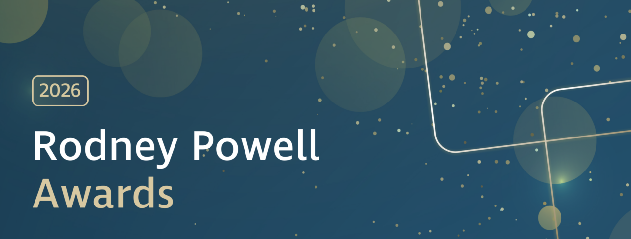 Graphic banner with a dark blue background featuring soft, translucent circles and scattered gold dots. A gold-outlined rectangle containing the text ‘2026’ appears on the left. Large white and gold text reads ‘Rodney Powell Awards.’ Decorative curved gold lines run across the right side of the image.