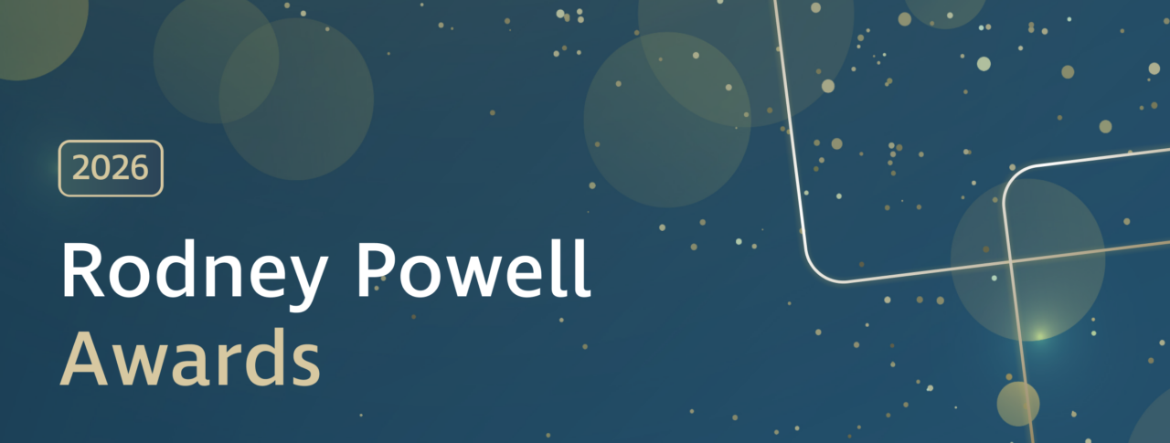 Graphic banner with a dark blue background featuring soft, translucent circles and scattered gold dots. A gold-outlined rectangle containing the text ‘2026’ appears on the left. Large white and gold text reads ‘Rodney Powell Awards.’ Decorative curved gold lines run across the right side of the image.