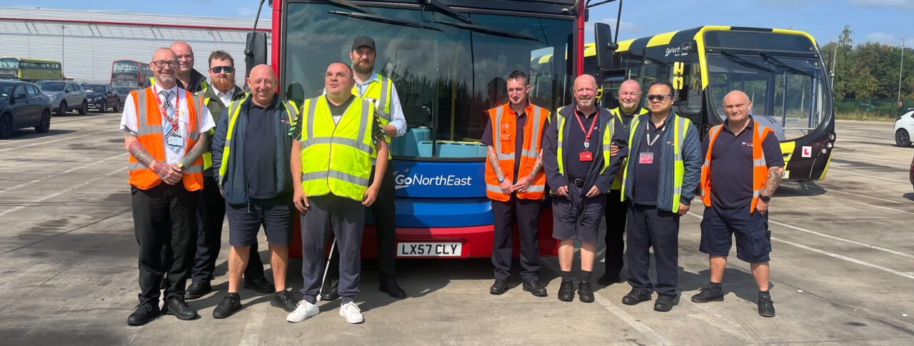 Darren, T&W SLC member, stood in front of a Go North East bus with Jack Moffat, Engagement Manager for NE England, and nine bus drivers. Everyone is wearing hi-vis jackets and smiling at the camera.