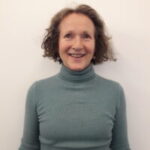 Headshot of Ann Griffin, North London SLC member. She has jaw length, brown, wavy hair. She is wearing a grey polo neck and smiling at the camera.