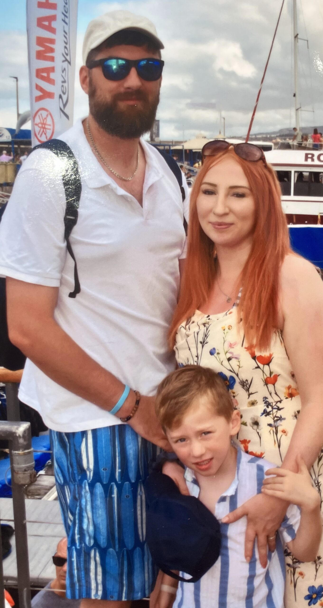 ack, Becky and Finlay on holiday. Jack is wearing a baseball cap and sunglasses. Behind them are the sails of several boats.