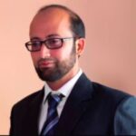 Mohammed Salman Shaikh headshot. Mohammed has short black hair and is wearing glasses, a black suit and white shirt with a navy tie. He is smiling at the camera.