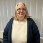 Photo of Tanja, Staffordshire Sight Loss Council member. Tanja has shoulder-length, fair hair and is wearing dark rimmed glasses. She is wearing a cream knitted top beneath a dark cardigan, and is smiling at the camera.