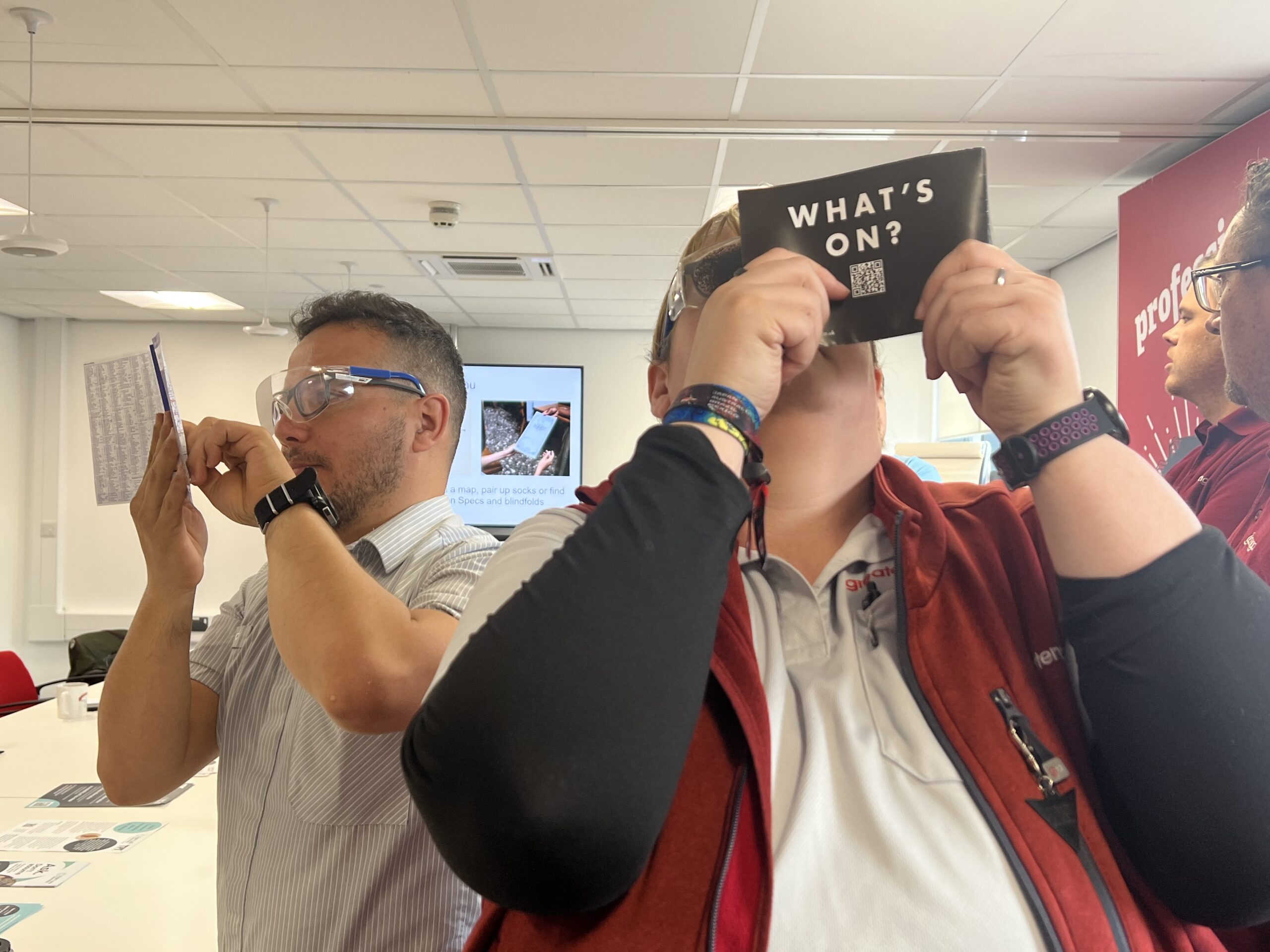 Two make staff members, wearing sim specs and holding small maps up in front of their faces, trying to read the information. This task is designed to highlight how tricky it can be to decipher information with a visual impairment. 