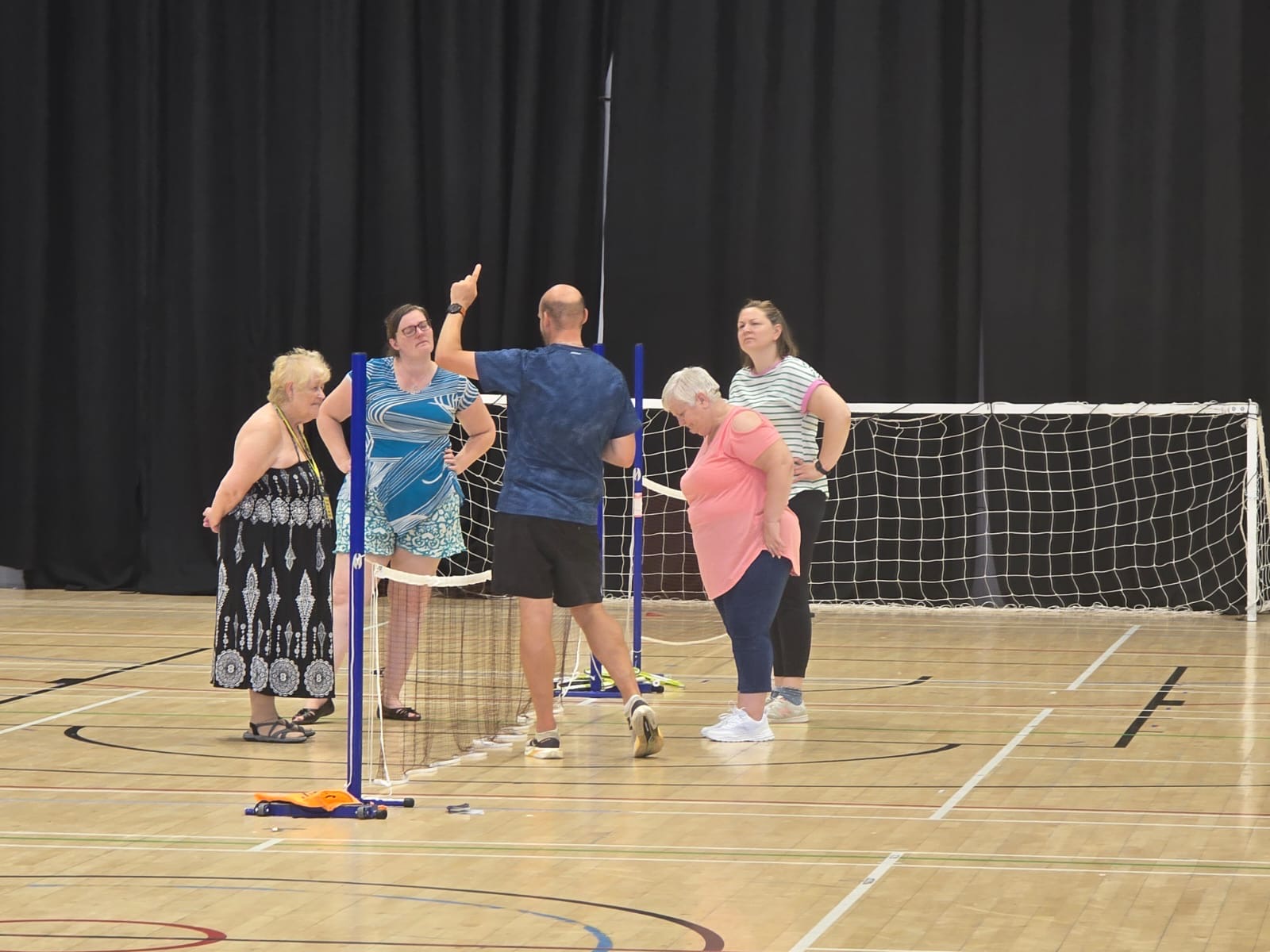 Four females listening to a coach at a tennis net in a sports hall, during South Yorkshire SLC's Let's Get Active Event