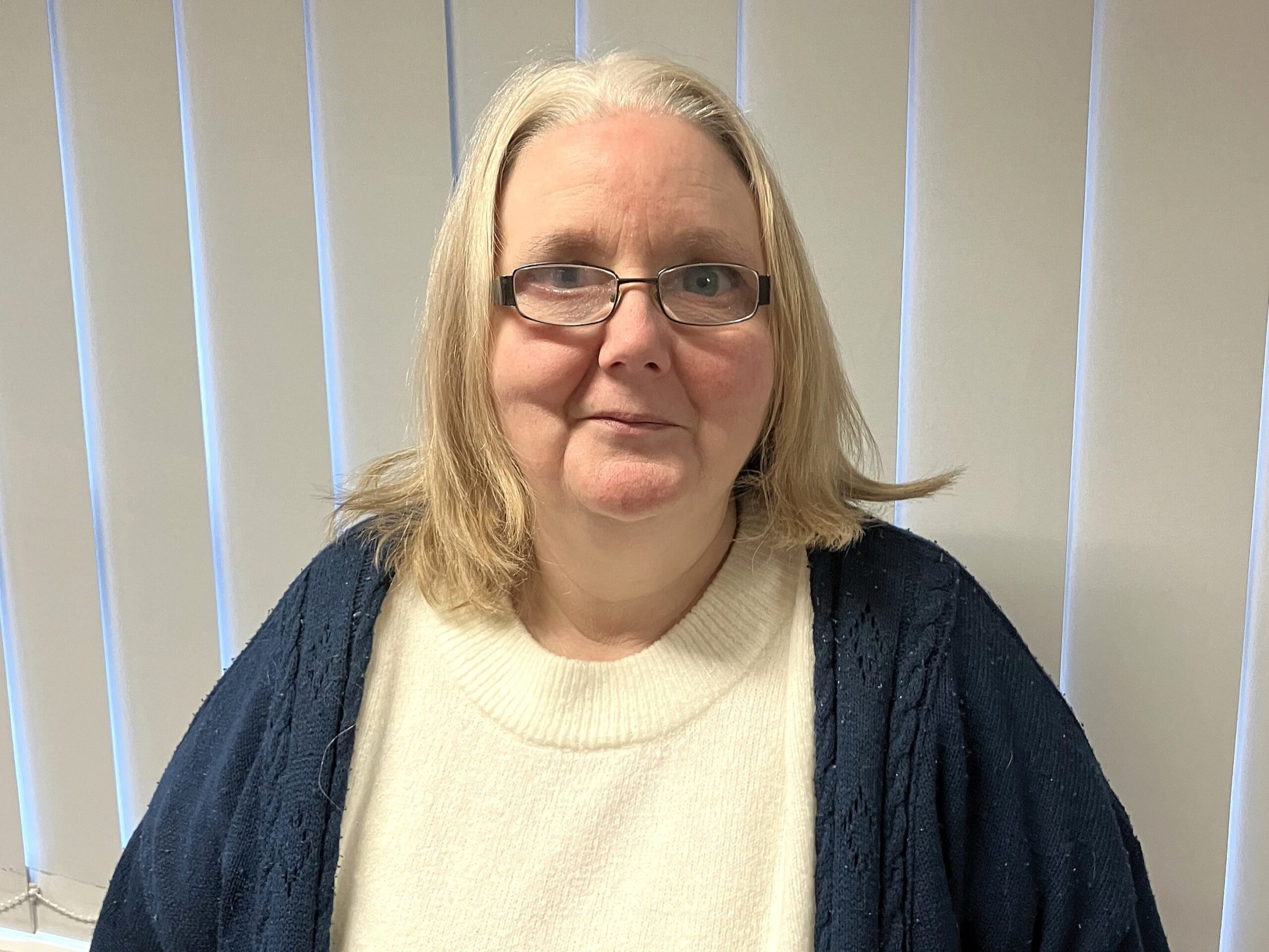 Photo of Tanja, Staffordshire Sight Loss Council member. Tanja has shoulder-length, fair hair and is wearing dark rimmed glasses. She is wearing a cream knitted top beneath a dark cardigan, and is smiling at the camera.