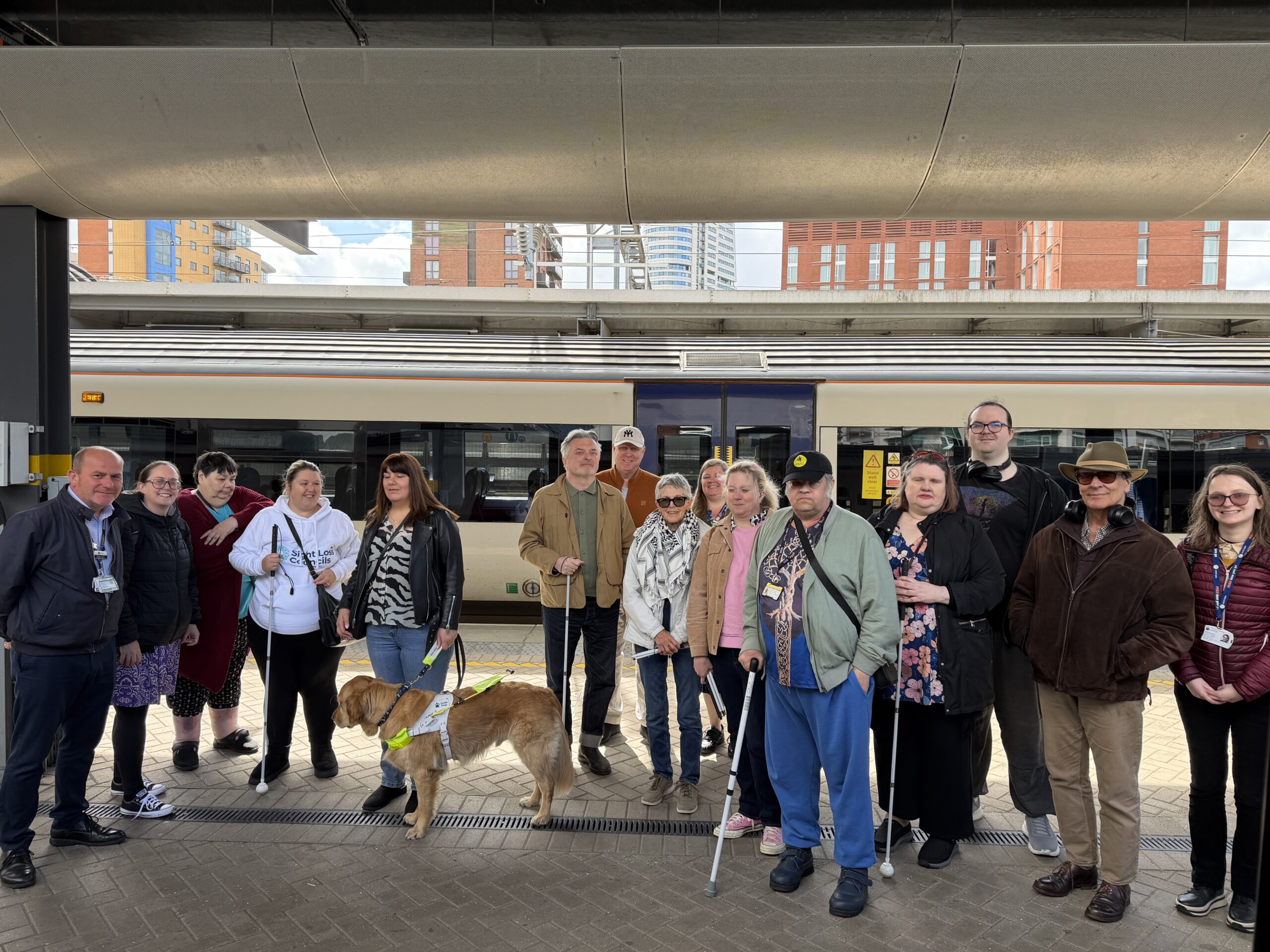 A group photo of blind and partially sighted participants and volunteers on a station platform during West Yorkshire SLC's recent Try a Train event A train is visible in the background.