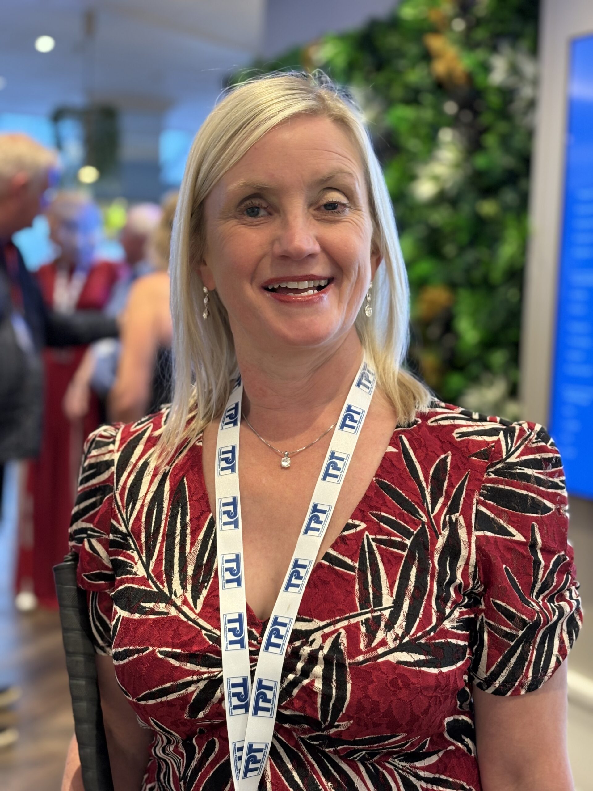 Closeup photo of Kelly Barton, Engagement Manager for North West England, taken at the 2026 SLC Conference. Kelly has shoulder length, blond hair. She is wearing a dark pink and black dress, and is smiling at the camera.