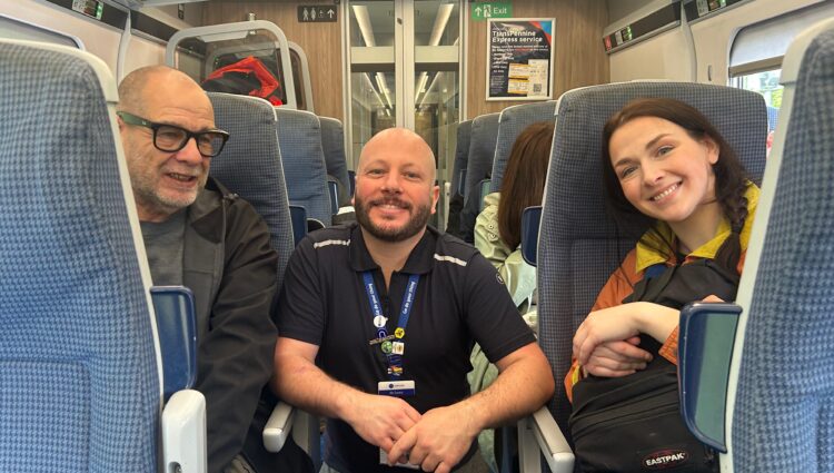 Mick, Sight Loss Council member, seated inside a train during a Try a Train event, alongside a Northern staff member and Community Rail Lancashire volunteer. All are smiling towards the camera.
