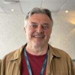 Close-up portrait of Toby, West Yorkshire Sight Loss Councils volunteer. He is wearing a Sight Loss Councils lanyard, and stands indoors against a softly lit background.