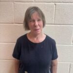 Photo of Lancashire SLC member, Lynn Williams. Lynn is stood against a white, brick wall. She has a short, dark, bob hairstyle and is wearing a black t-shirt. She is smiling towards the camera.