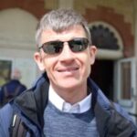 Headshot of Dave Smith, Engagement Manager for South East England. The photo is taken outside a railway station. Dave is wearing dark sunglasses, and smiling at the camera.