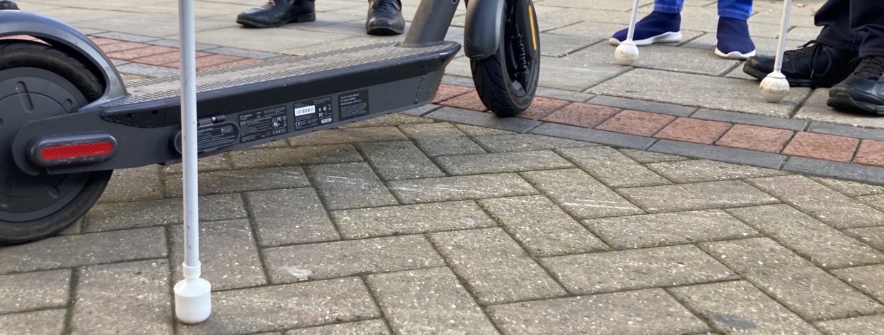 feet and white canes surrounding an e-scooter