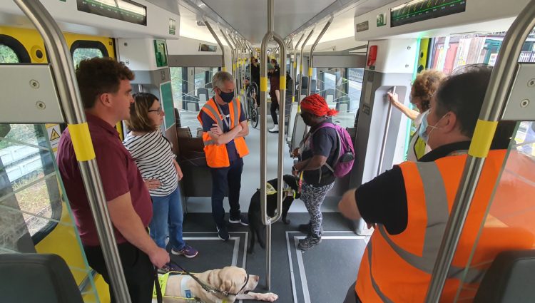 A group of people inside a train, some are guide dog users, some are wearing high-vis vests.