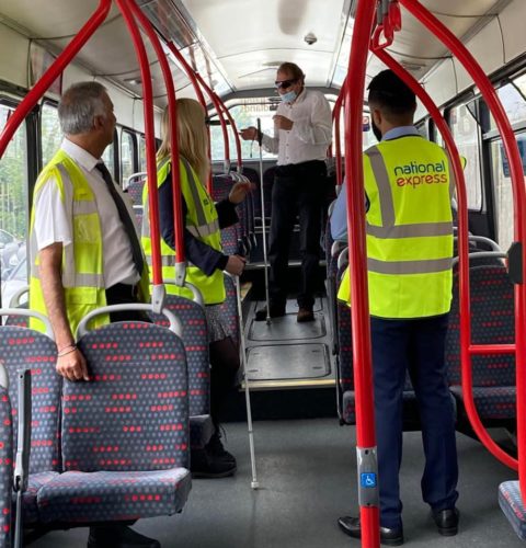 A group of people wearing hi-vis jackets are aboard a bus, some of whom are white cane users.