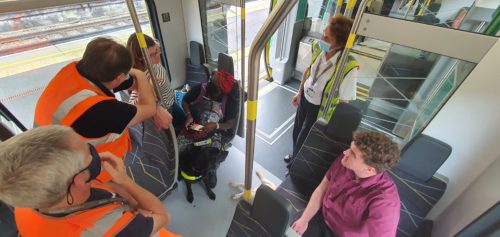 A group of people inside a train, some are guide dog users, some are wearing high-vis vests.