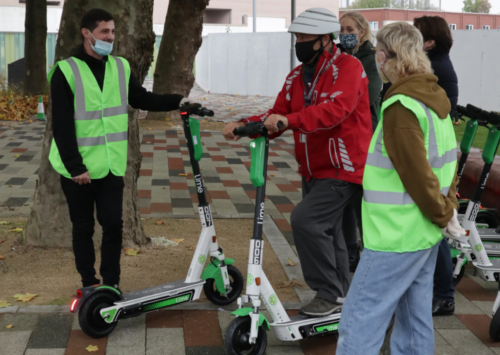 three people inspecting two Lime e-scooters