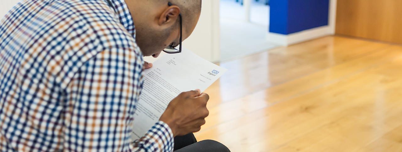 Man wearing glasses struggling to read NHS letter