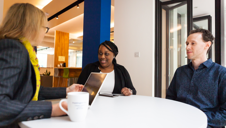 Three people in business attire sat around roundtable