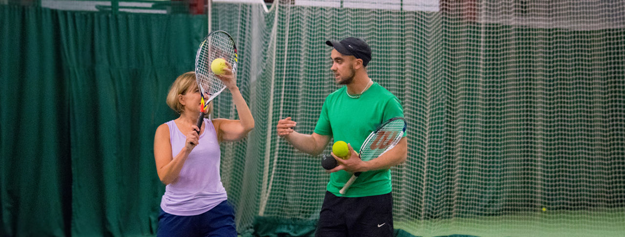 player learning to serve with tennis coach on her right