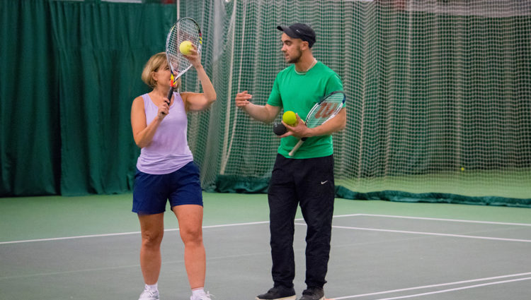 player learning to serve with tennis coach on her right