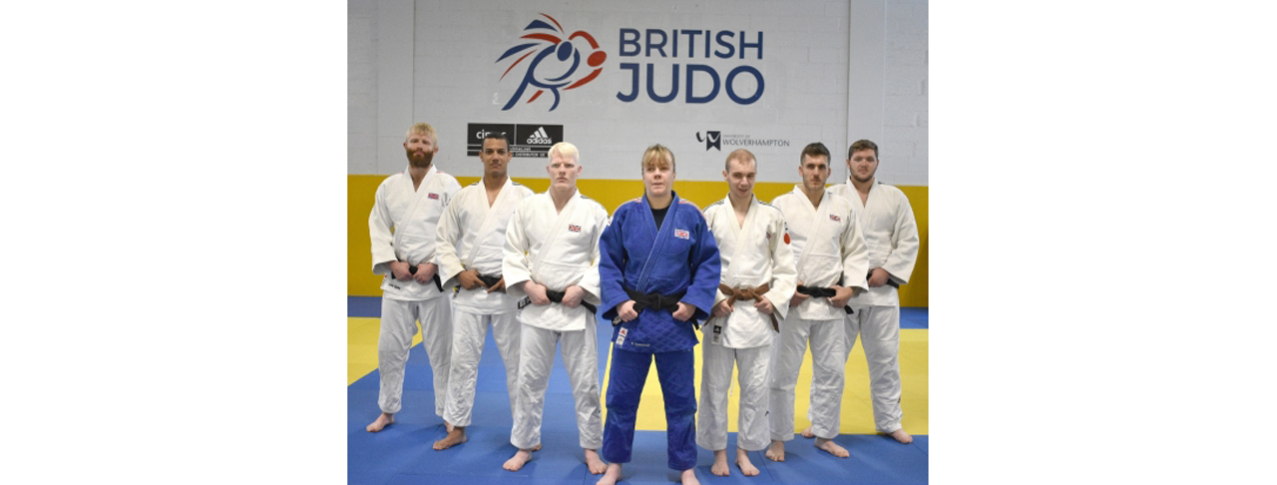 natalie standing at the front of 6 other judo teammates with the British logo in the background