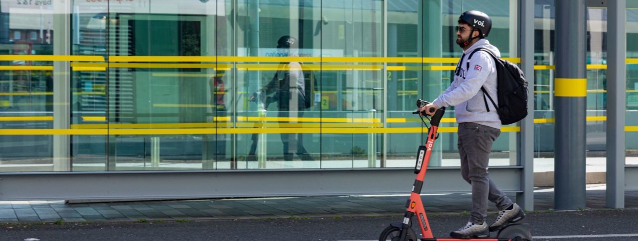 Man riding an e-scooter past a bus stop