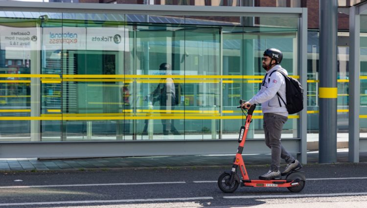 Man riding an e-scooter past a bus stop