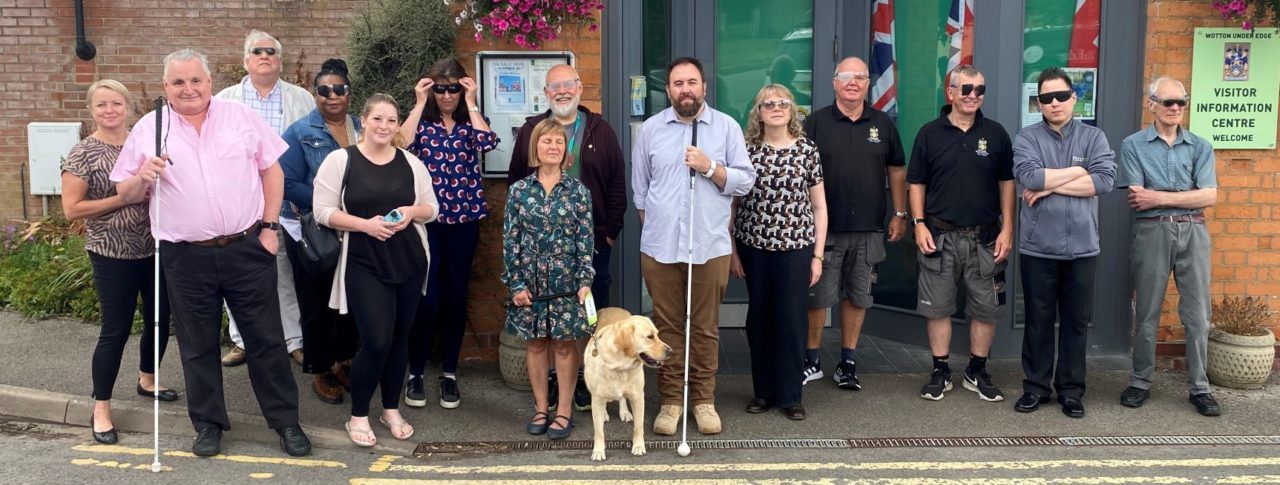 Council leaders stood with Gloucestershire Sight Loss Council members outside Wotton Museum and Heritage Centre. Council leaders are wearing simulation spectacles. Left to right: District Cllr Natalie Bennett (Chair of Stroud District Council's EDI Working Group), Alun Davies (GSLC), District Cllr Ken Tucker, Elaine Gordon, Louisa Sanderson and Eka Nowakowska (SDC Officers), District Cllr Robin Layfield, Julie Stephens (GLSC), Wayne Hands (GLSC), Diana Hyam, Phil Wilson and Andy Burns (WuE Town Council), Town Councillors Jon Turner and Roger