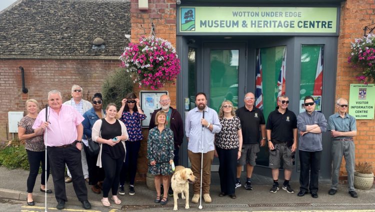 Council leaders stood with Gloucestershire Sight Loss Council members outside Wotton Museum and Heritage Centre. Council leaders are wearing simulation spectacles. Left to right: District Cllr Natalie Bennett (Chair of Stroud District Council's EDI Working Group), Alun Davies (GSLC), District Cllr Ken Tucker, Elaine Gordon, Louisa Sanderson and Eka Nowakowska (SDC Officers), District Cllr Robin Layfield, Julie Stephens (GLSC), Wayne Hands (GLSC), Diana Hyam, Phil Wilson and Andy Burns (WuE Town Council), Town Councillors Jon Turner and Roger