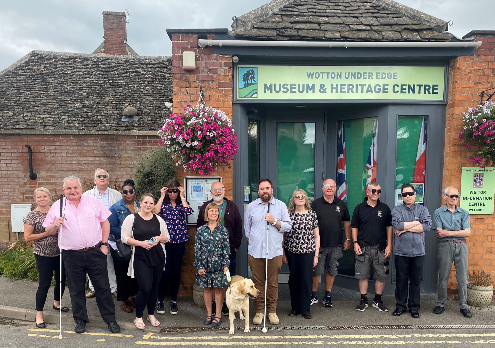 Council leaders stood with Gloucestershire Sight Loss Council members outside Wotton Museum and Heritage Centre. Council leaders are wearing simulation spectacles. Left to right: District Cllr Natalie Bennett (Chair of Stroud District Council's EDI Working Group), Alun Davies (GSLC), District Cllr Ken Tucker, Elaine Gordon, Louisa Sanderson and Eka Nowakowska (SDC Officers), District Cllr Robin Layfield, Julie Stephens (GLSC), Wayne Hands (GLSC), Diana Hyam, Phil Wilson and Andy Burns (WuE Town Council), Town Councillors Jon Turner and Roger