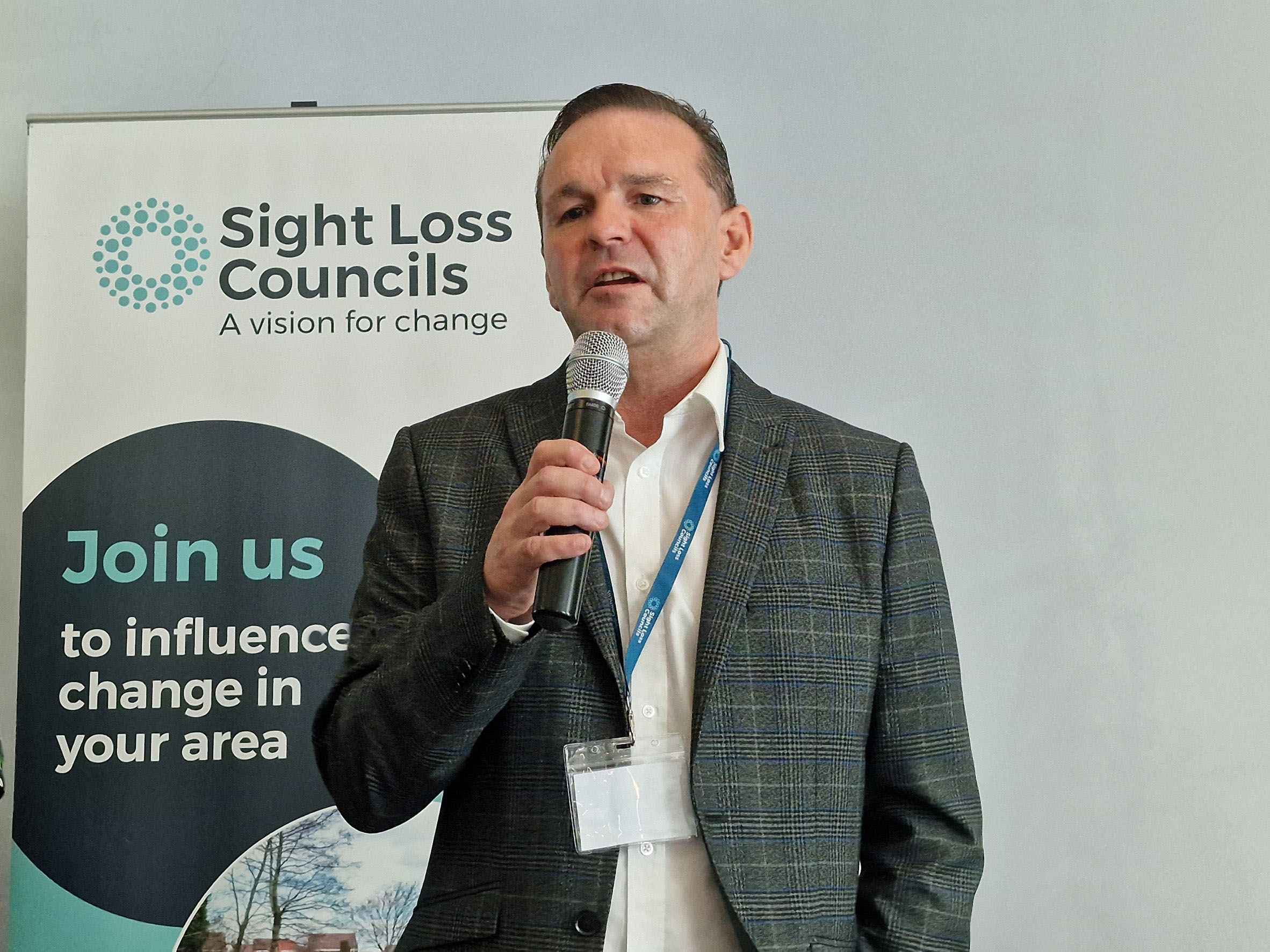 Image shows Sight Loss Council member Paul giving his talk about getting back into work after losing his sight. He is stood in front of a Sight Loss Council banner.
