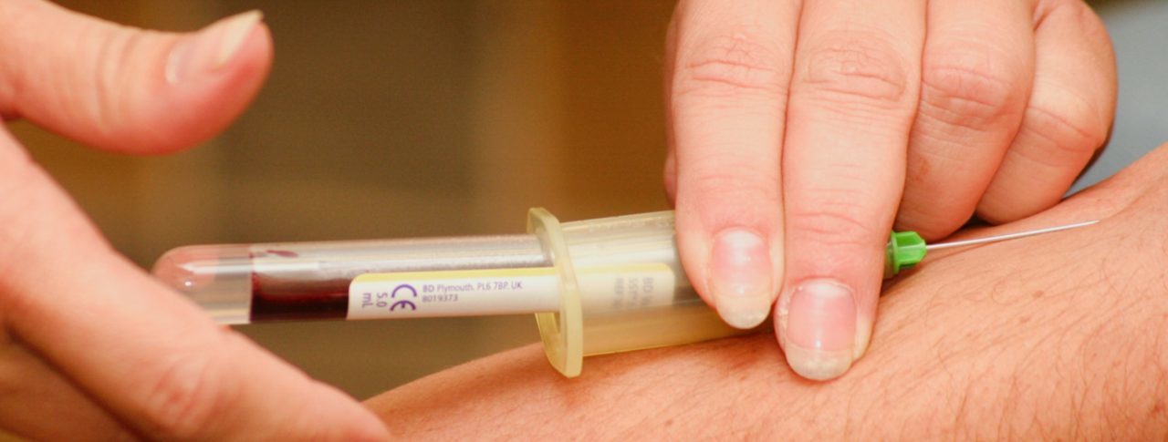 Blood is being drawn out of an arm using a syringe