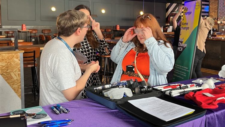Retailer trying on simulation spectacles, stood with Sight Loss Council members at their stall.