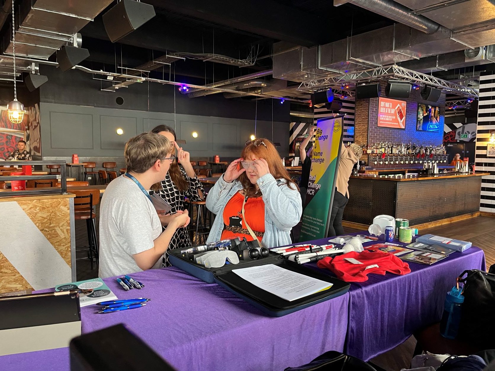 Retailer trying on simulation spectacles, stood with Sight Loss Council members at their stall.