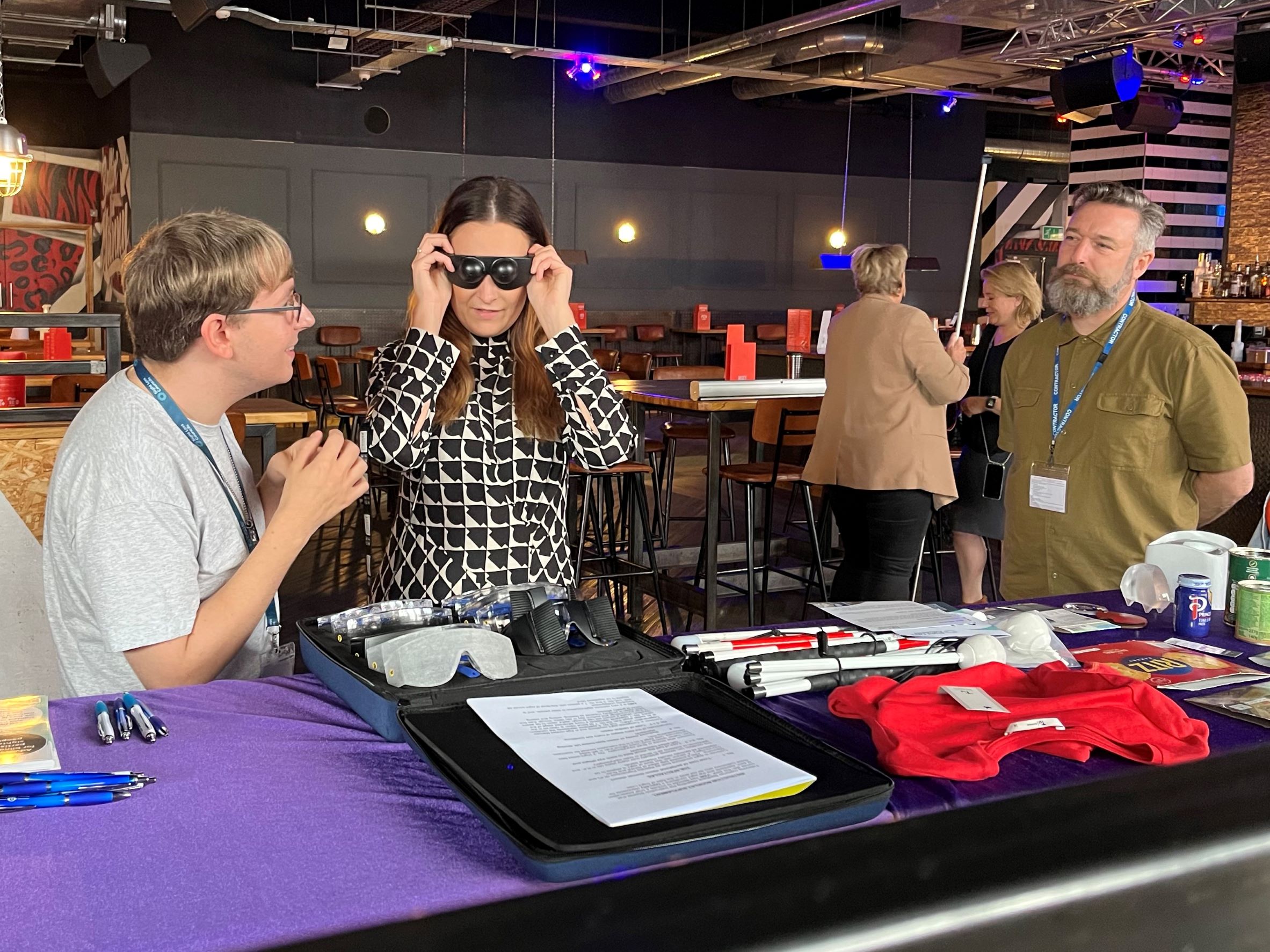 Staff member tries on simulation glasses to experience different eye conditions. They are pictured with a Sight Loss Council member at their stall.