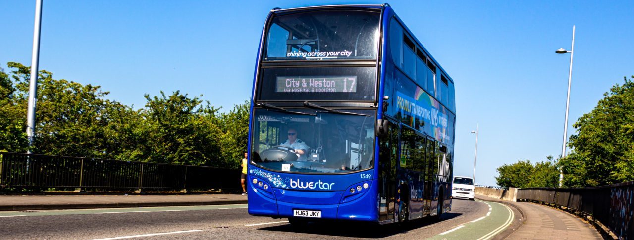 A bus blue makes it's way along a sun drenched road towards the City and Weston hospital in Bristol