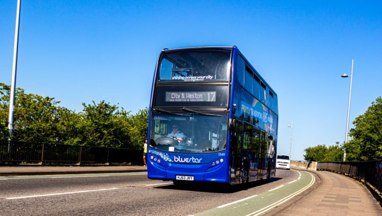 A bus blue makes it's way along a sun drenched road towards the City and Weston hospital in Bristol