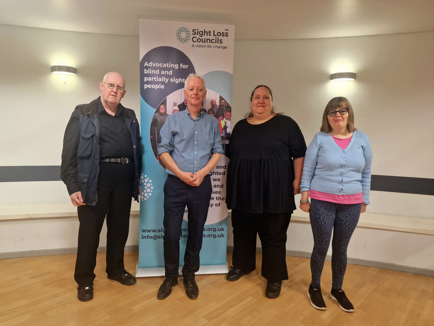 Image shows three Sight Loss Council (SLC) members with Engagement Manager Eamonn at the event, stood infront of a Sight Loss Council banner. Left to right: SLC member Martin, Engagement Manager Eamonn, and SLC members Hazel and Toni