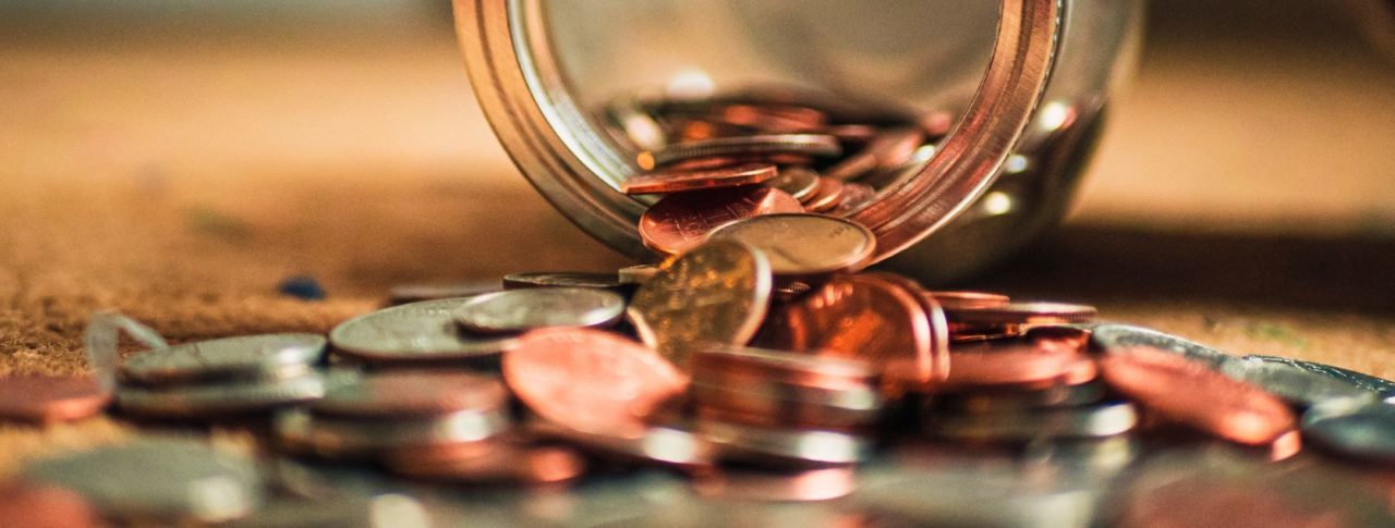 Glass jar of coins, spilling out onto a table.