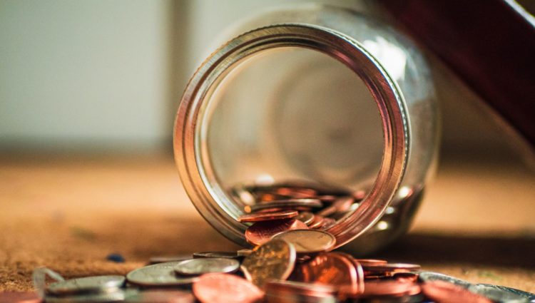 Glass jar of coins, spilling out onto a table.