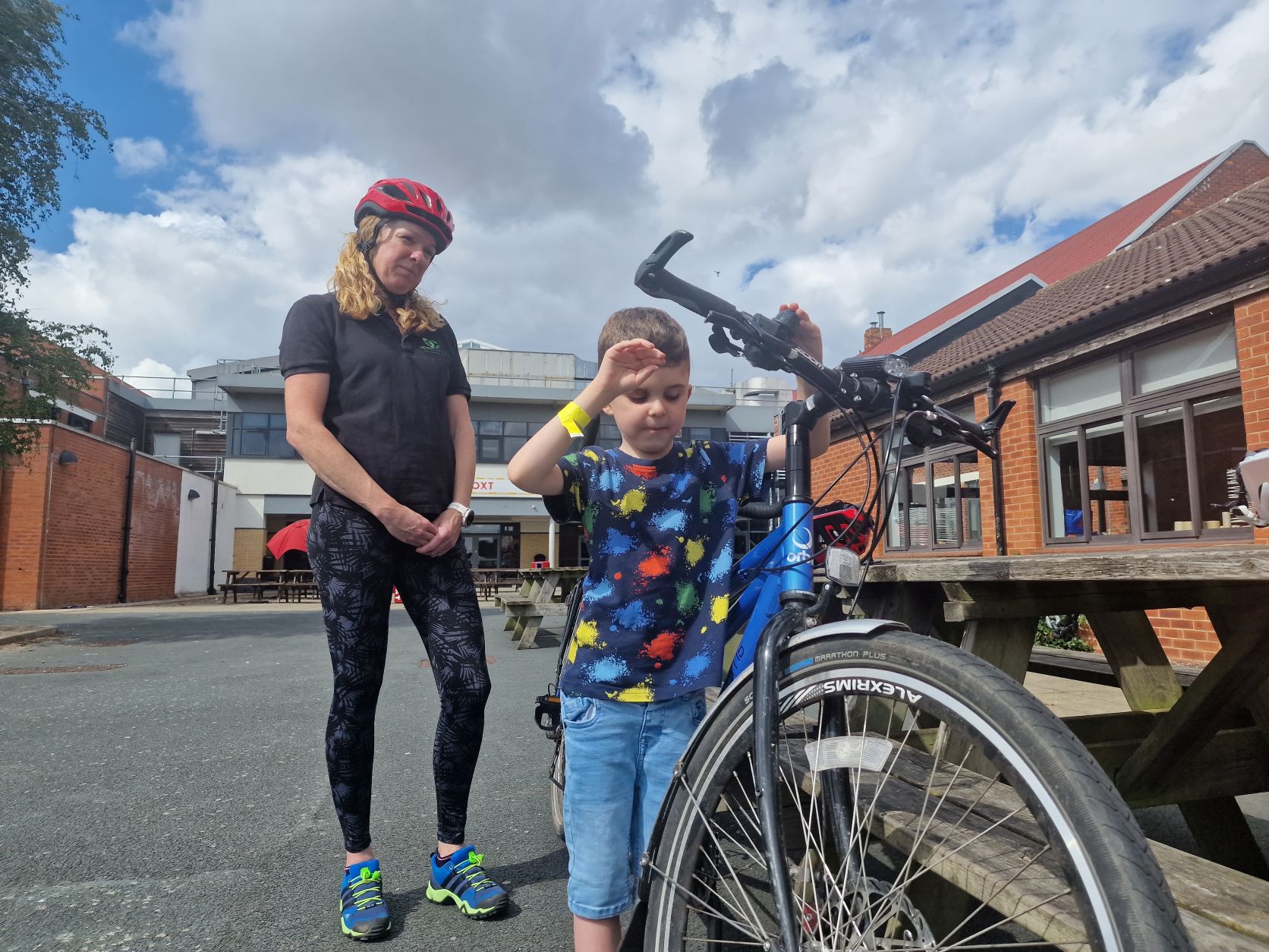 Image shows young bout Teddy, standing at a bicycles handlebars. Tandem coach Lizzie is standing behind him.