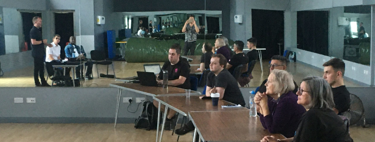 Image shows Wave Leisure Trust staff sat at tables listening to the training being delivered by Thomas Pocklington Trust’s Head of Sport and Leisure, Martin Symcox. Dave Smith, South East SLC Engagement Manager, and East Sussex SLC member Cyril Thomas, who supported the sessions, are sat next to him