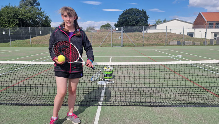 Lydia Wrightson, Ladies B4 Single Champion at the National VI Tennis Championships and a supporter coach at the event, stood in a tennis court holding a racket and ball.