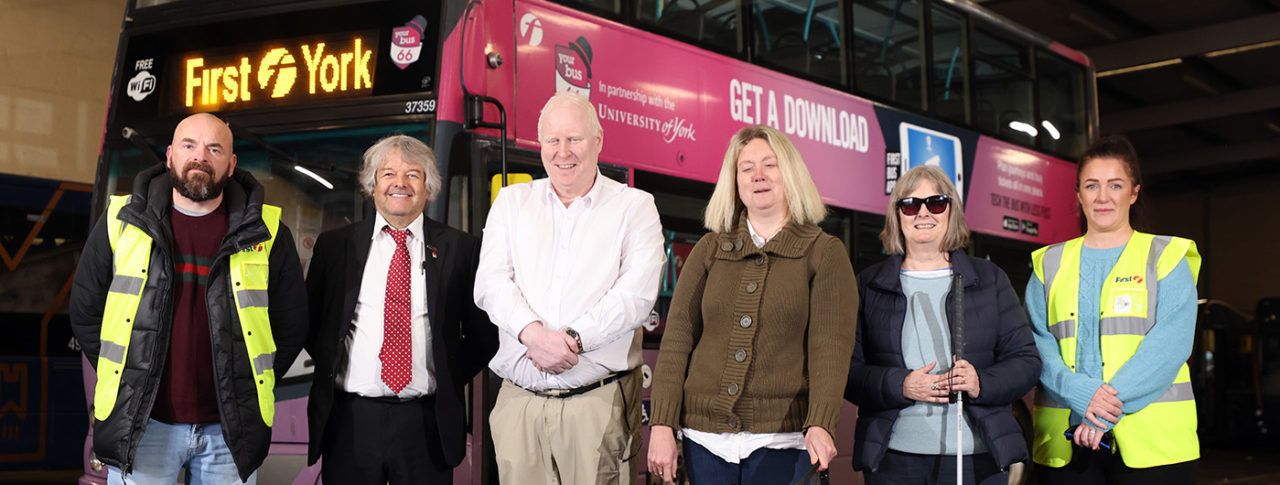 Left to right: Trainee driver Richard Ward, Training and Recruitment Manager Keith Sheard and Trainee Driver Chantelle Pisarkeiwicz. They are stood in a line in front of a red First York bus. They are smiling.