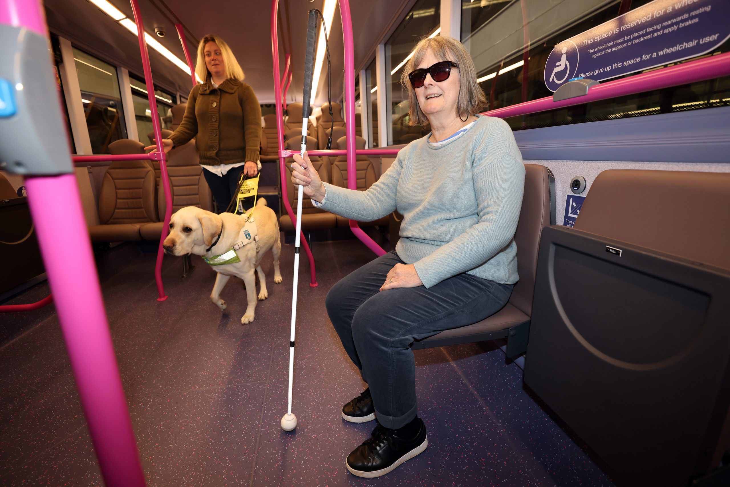 York Sight Loss Council members Verity (with her guide dog Ted) and Josie Clarke on a bus at the First Bus - York bus depot training school 19 October 2022. Josie is sat on a seat and holding a white cane. Verity is walking down the centre of the bus with her guide dog.
