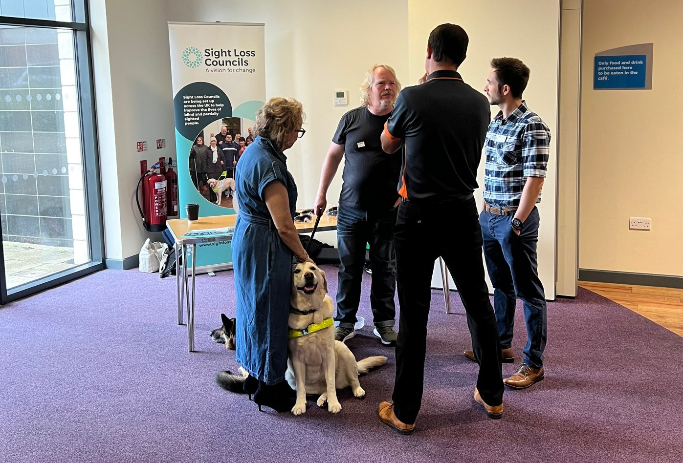 Birmingham SLC members and Places Leisure staff standing in a circle, deep in conversation. A lady is holding her guide dog.