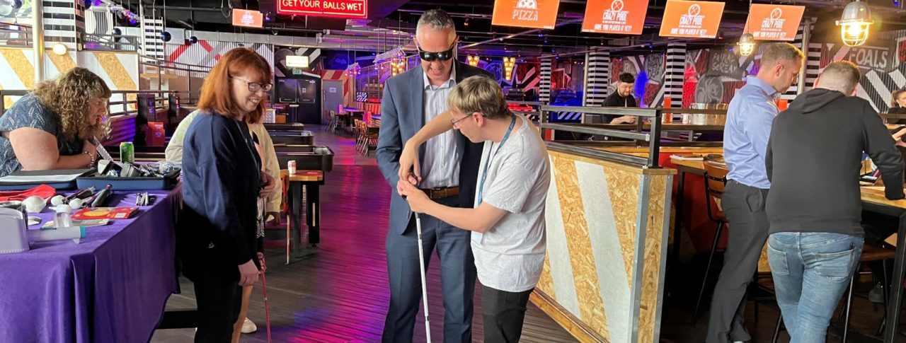 Retailer wearing simulation glasses and holding a cane with a Sight Loss Council member